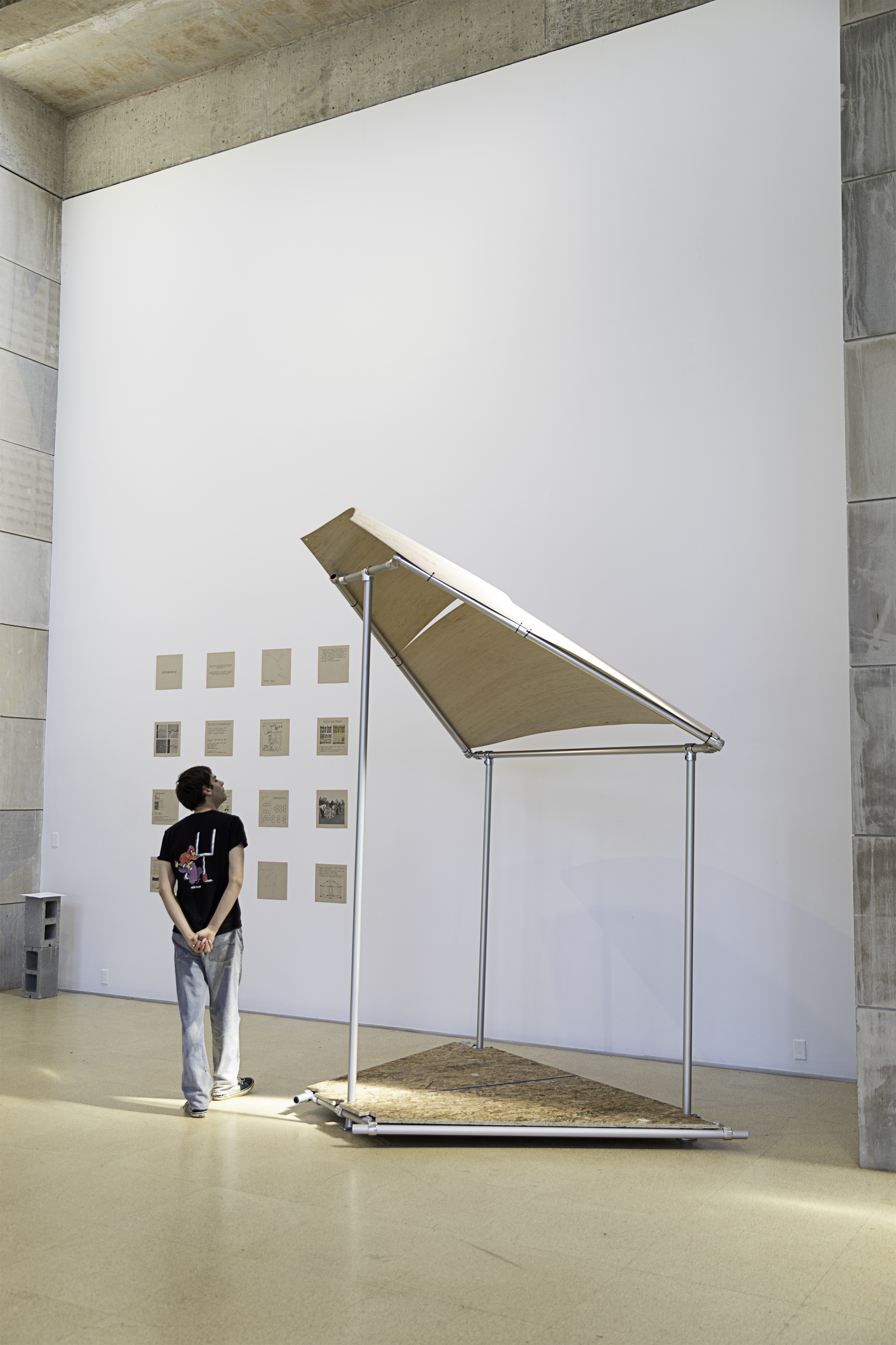 A man looks up at a built happenspace module in a brightly-lit gallery space.